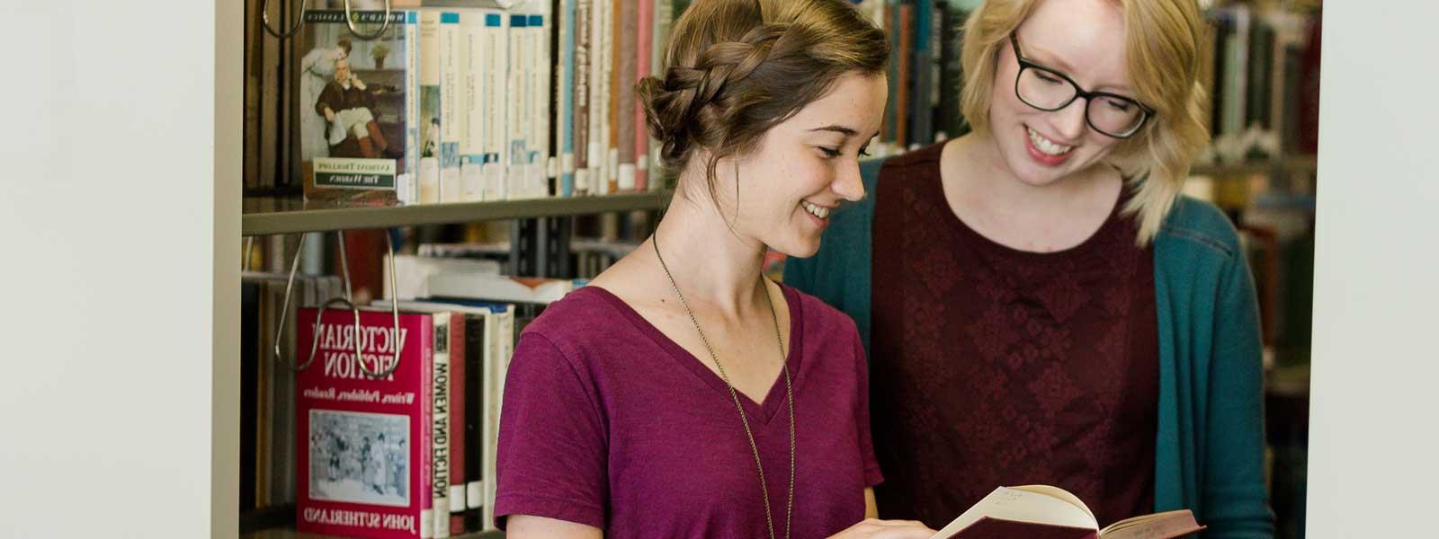 two students look at book in library
